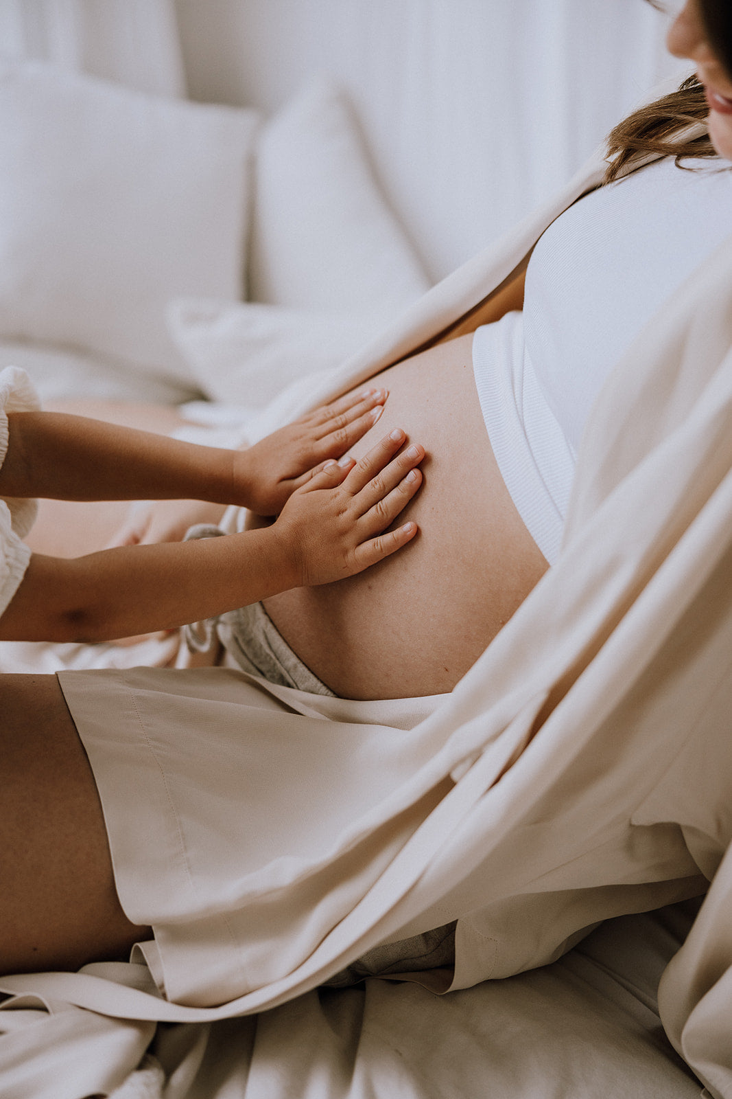 Et barn lægger hænderne på en gravid mave, mens personen sidder på en sofa.