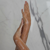 Hænder masserer kropsscrub ind på våd hud i badet.