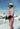 Person i lyserødt skitøj med hjelm og skibriller står på ski i sneklædt bjerglandskab under blå himmel.