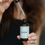 Person holder hårserum “Grow” fra Cana Care og løfter pipetten med en dråbe serum over flasken.